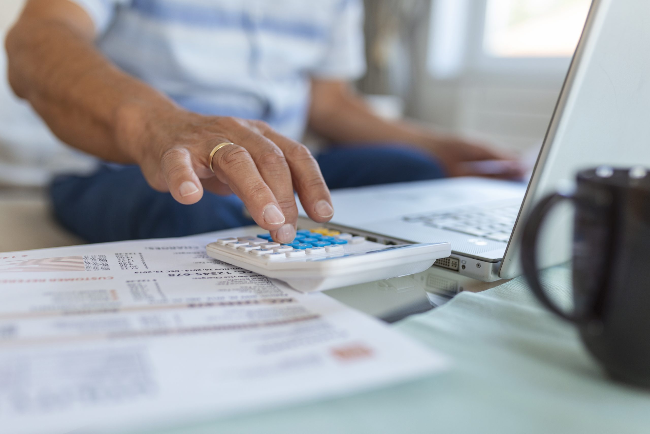 Serious elder senior grey-haired grandpa using calculator counting bank loan payment holding papers at home, focused mature old man doing paperwork calculating bills managing finances sit on sofa